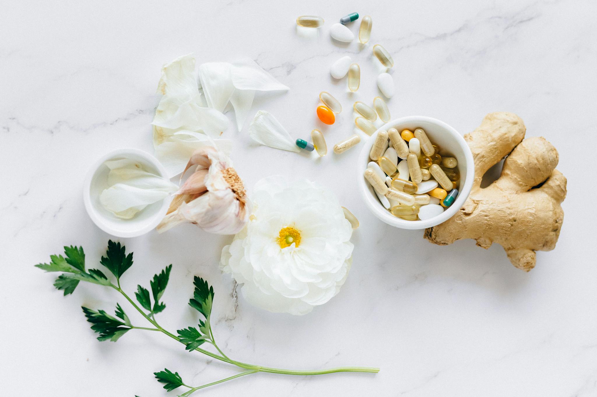 Top view of herbal medicine and supplements with ginger, flower, and capsules on a white background.